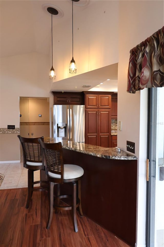 kitchen with stone countertops, hardwood / wood-style floors, pendant lighting, stainless steel fridge, and kitchen peninsula