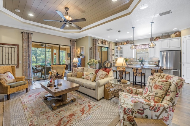 living room with a tray ceiling, light wood-type flooring, and ornamental molding