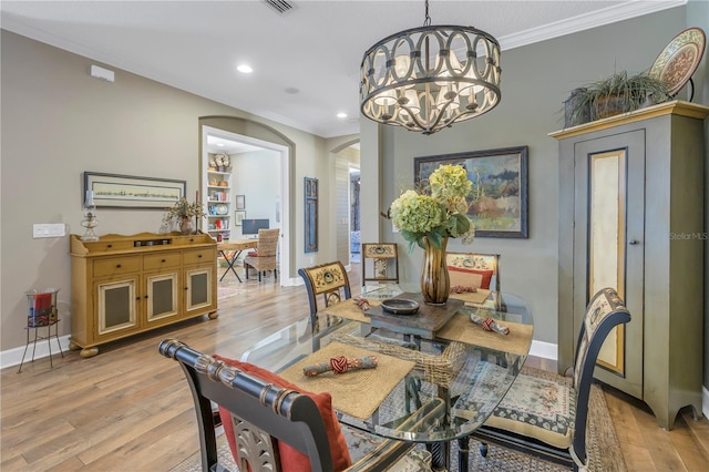 dining space with an inviting chandelier, ornamental molding, and light wood-type flooring