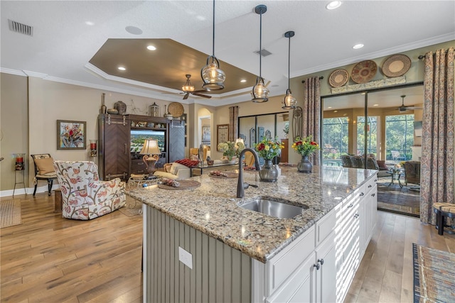 kitchen featuring sink, light stone countertops, light wood-type flooring, an island with sink, and white cabinetry