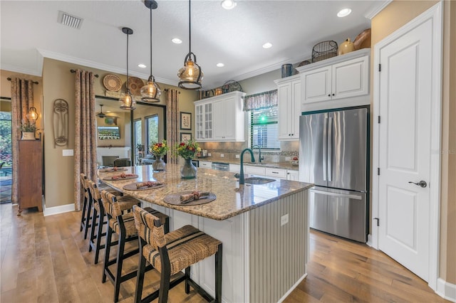 kitchen with sink, ornamental molding, an island with sink, appliances with stainless steel finishes, and light stone counters