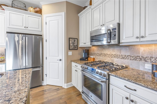 kitchen with stainless steel appliances, tasteful backsplash, light stone counters, light hardwood / wood-style flooring, and white cabinets