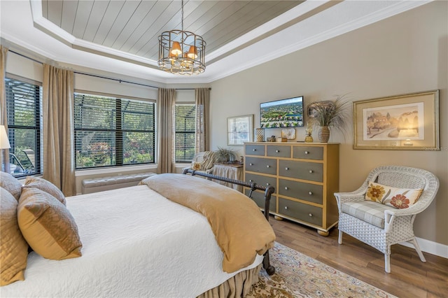 bedroom with hardwood / wood-style floors, an inviting chandelier, a raised ceiling, and ornamental molding