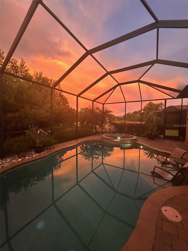 pool at dusk with glass enclosure, a patio area, and an in ground hot tub