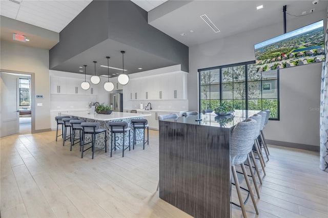 kitchen featuring stainless steel fridge, a spacious island, pendant lighting, white cabinets, and a high ceiling