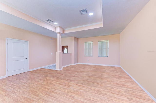 spare room featuring a textured ceiling, light wood-type flooring, and a tray ceiling