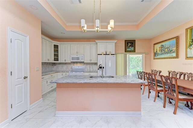 kitchen featuring a tray ceiling, light stone counters, hanging light fixtures, and white appliances