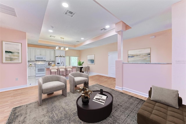 living room featuring a notable chandelier, a raised ceiling, and light hardwood / wood-style flooring