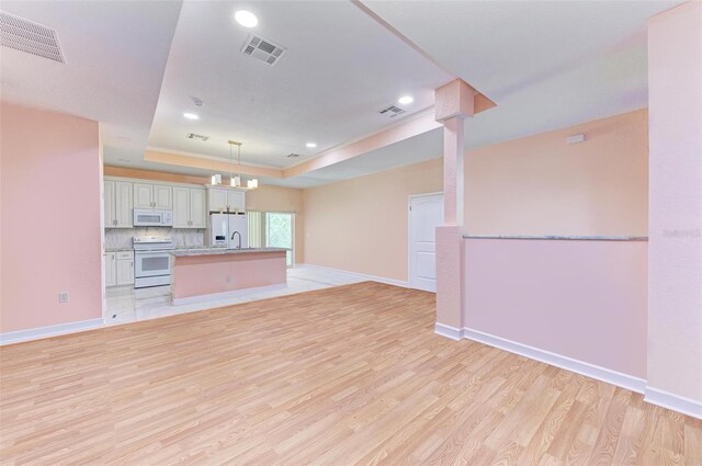 unfurnished living room with a tray ceiling, sink, light hardwood / wood-style floors, and a notable chandelier