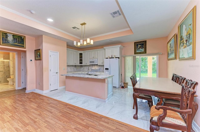 kitchen featuring white cabinetry, light stone counters, an island with sink, decorative light fixtures, and white appliances