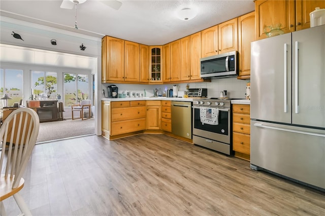 kitchen with decorative backsplash, appliances with stainless steel finishes, ceiling fan, sink, and light hardwood / wood-style floors