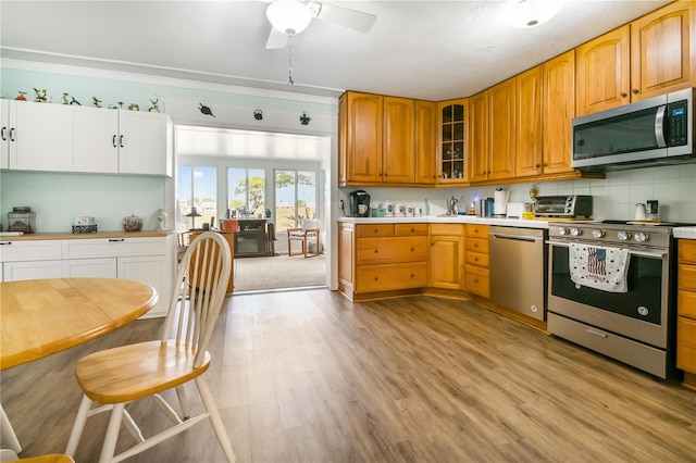 kitchen with tasteful backsplash, appliances with stainless steel finishes, light hardwood / wood-style floors, and ceiling fan