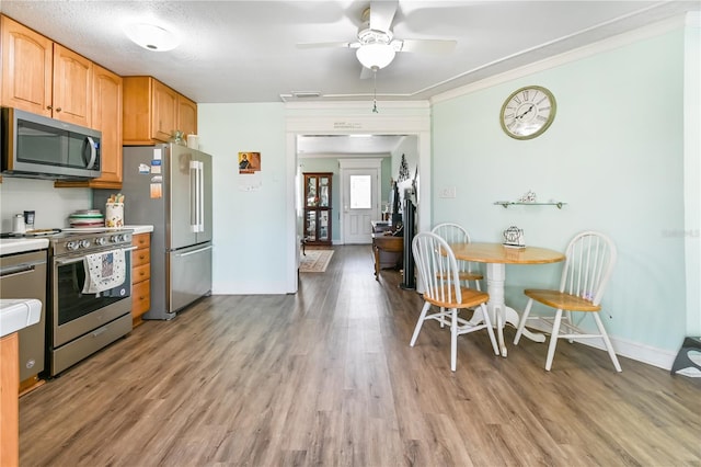 kitchen featuring ceiling fan, crown molding, light hardwood / wood-style floors, a textured ceiling, and appliances with stainless steel finishes