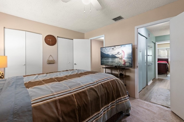 bedroom with multiple closets, ceiling fan, hardwood / wood-style floors, and a textured ceiling