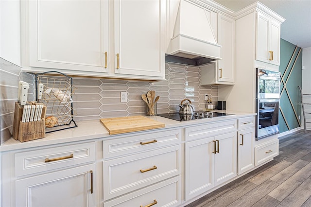 kitchen with double oven, hardwood / wood-style floors, black electric cooktop, white cabinets, and custom range hood