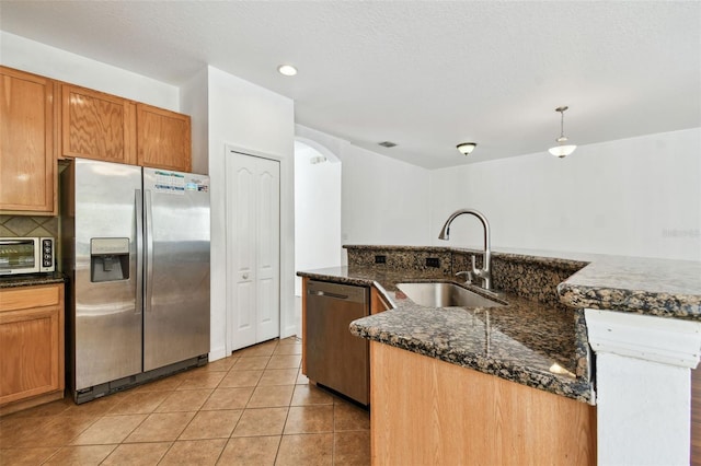 kitchen with appliances with stainless steel finishes, dark stone counters, sink, pendant lighting, and light tile patterned flooring