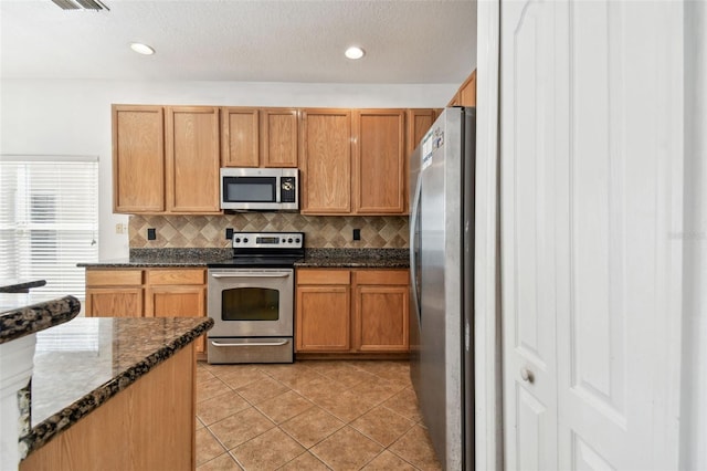 kitchen featuring backsplash, a textured ceiling, stainless steel appliances, light tile patterned floors, and dark stone countertops