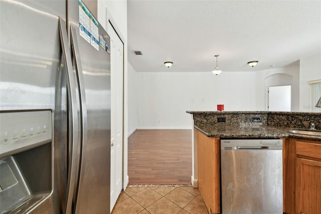 kitchen featuring sink, stainless steel appliances, dark stone counters, decorative light fixtures, and light hardwood / wood-style floors