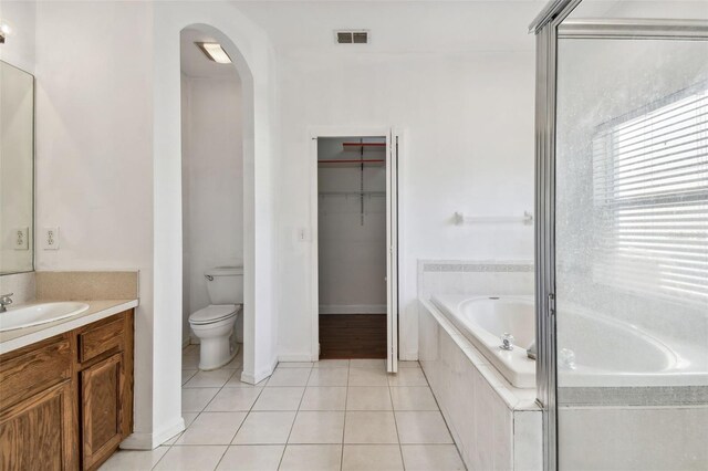 bathroom featuring tile patterned floors, vanity, a relaxing tiled tub, and toilet