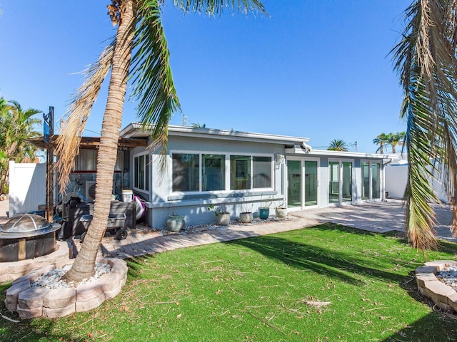 rear view of property with a sunroom, a patio area, a yard, and an outdoor fire pit