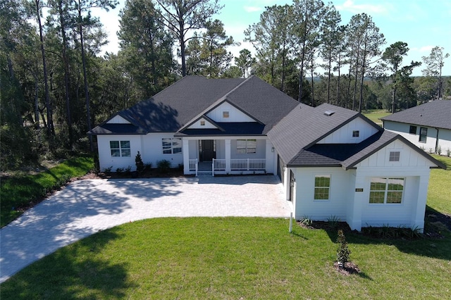 view of front of property with roof with shingles, a porch, board and batten siding, a front yard, and driveway