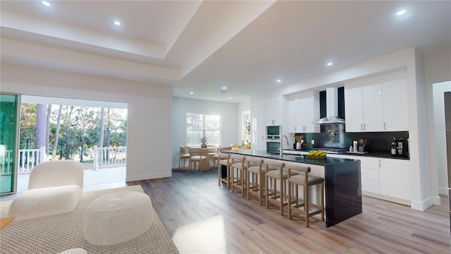 kitchen featuring white cabinets, wall chimney exhaust hood, light hardwood / wood-style floors, and plenty of natural light