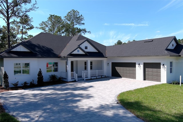 view of front of property featuring an attached garage, covered porch, a shingled roof, decorative driveway, and a front lawn