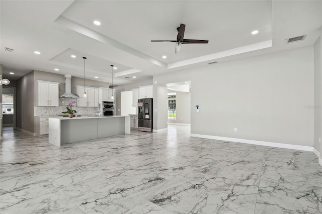 kitchen featuring a tray ceiling, white cabinetry, wall chimney range hood, and appliances with stainless steel finishes