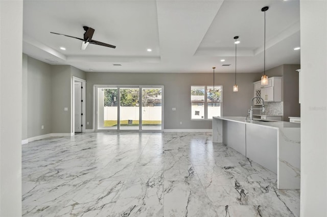 kitchen featuring ceiling fan, sink, a raised ceiling, decorative light fixtures, and white cabinets