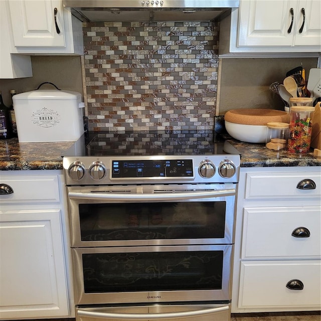 kitchen with tasteful backsplash, stainless steel electric range oven, dark stone countertops, white cabinetry, and range hood