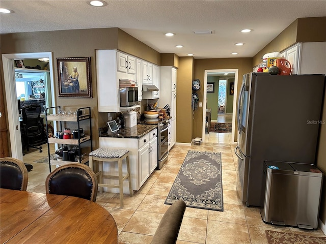 kitchen featuring stainless steel appliances, white cabinets, dark stone counters, a textured ceiling, and light tile patterned flooring