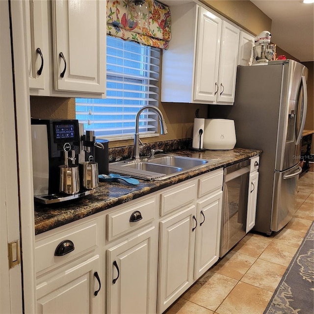 kitchen featuring dark stone countertops, appliances with stainless steel finishes, white cabinetry, and a sink