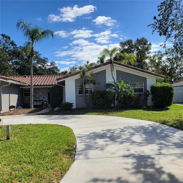 mid-century inspired home featuring a front lawn, a tile roof, driveway, and stucco siding