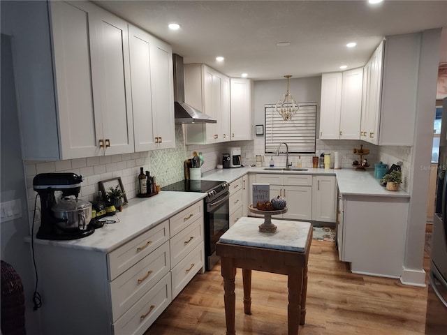 kitchen with electric stove, decorative light fixtures, white cabinetry, sink, and wall chimney exhaust hood