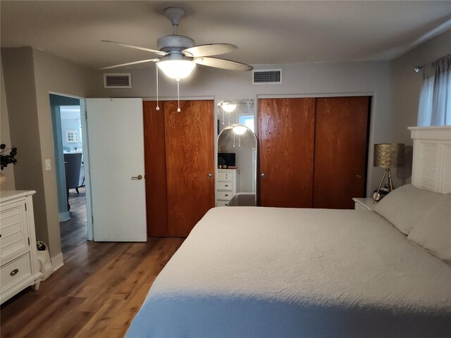 bedroom with ceiling fan, dark hardwood / wood-style flooring, and two closets