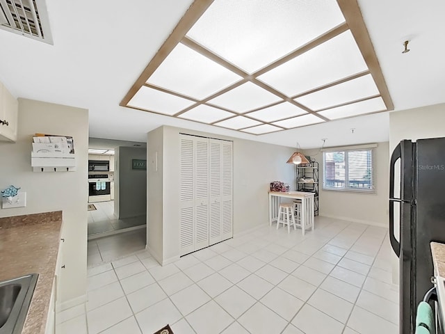 kitchen featuring light tile patterned floors, black appliances, and decorative light fixtures