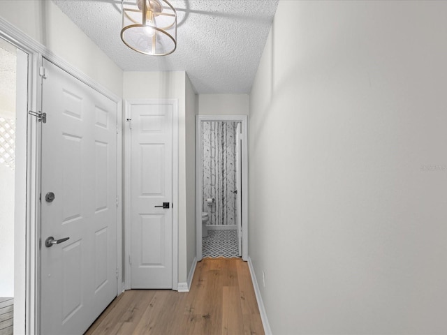 corridor with a textured ceiling and light wood-type flooring