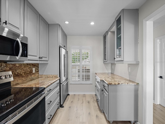 kitchen featuring gray cabinetry, light stone countertops, light wood-type flooring, and appliances with stainless steel finishes