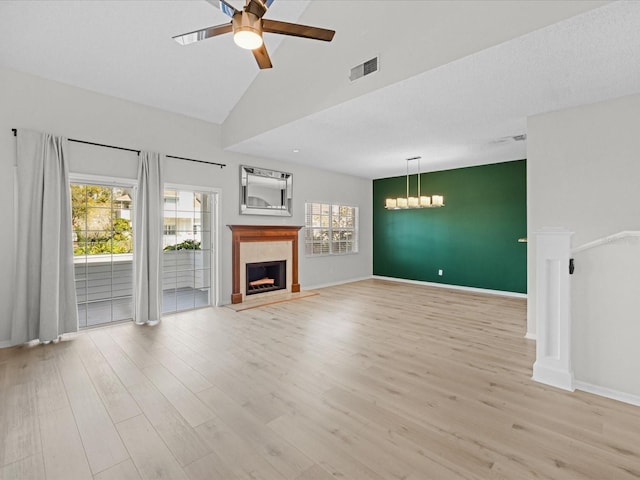 unfurnished living room featuring ceiling fan with notable chandelier, light wood-type flooring, high vaulted ceiling, and a healthy amount of sunlight