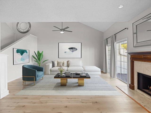 living room featuring light wood-type flooring, ceiling fan, lofted ceiling, and a tiled fireplace