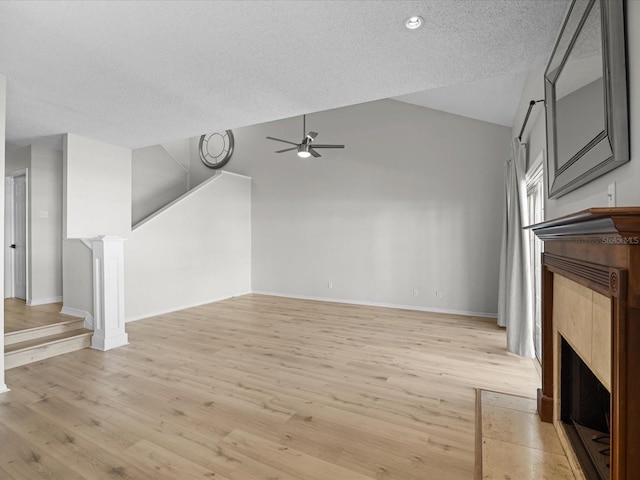 unfurnished living room with vaulted ceiling, light hardwood / wood-style flooring, ceiling fan, a textured ceiling, and a fireplace