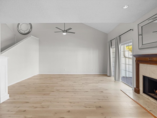 unfurnished living room featuring a textured ceiling, vaulted ceiling, ceiling fan, a tile fireplace, and light hardwood / wood-style floors