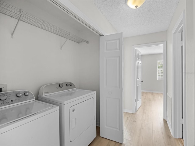 clothes washing area featuring washing machine and dryer, light wood-type flooring, and a textured ceiling