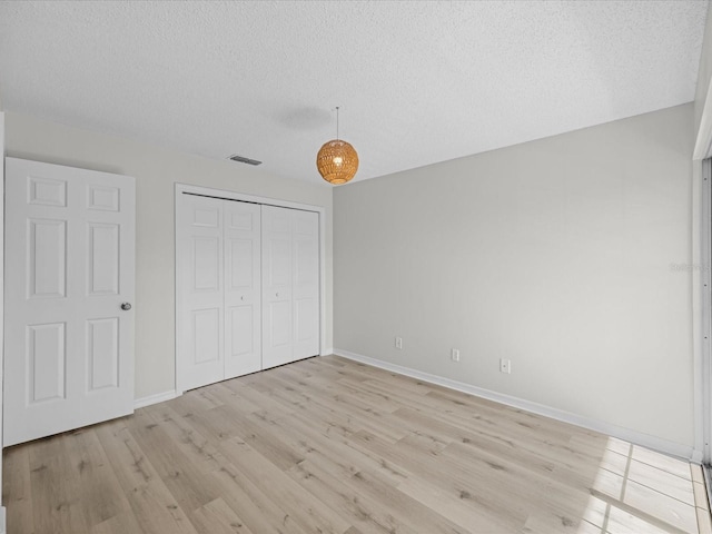 unfurnished bedroom featuring a textured ceiling, light hardwood / wood-style flooring, and a closet