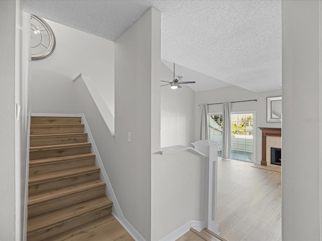 staircase featuring hardwood / wood-style flooring, ceiling fan, a textured ceiling, and vaulted ceiling