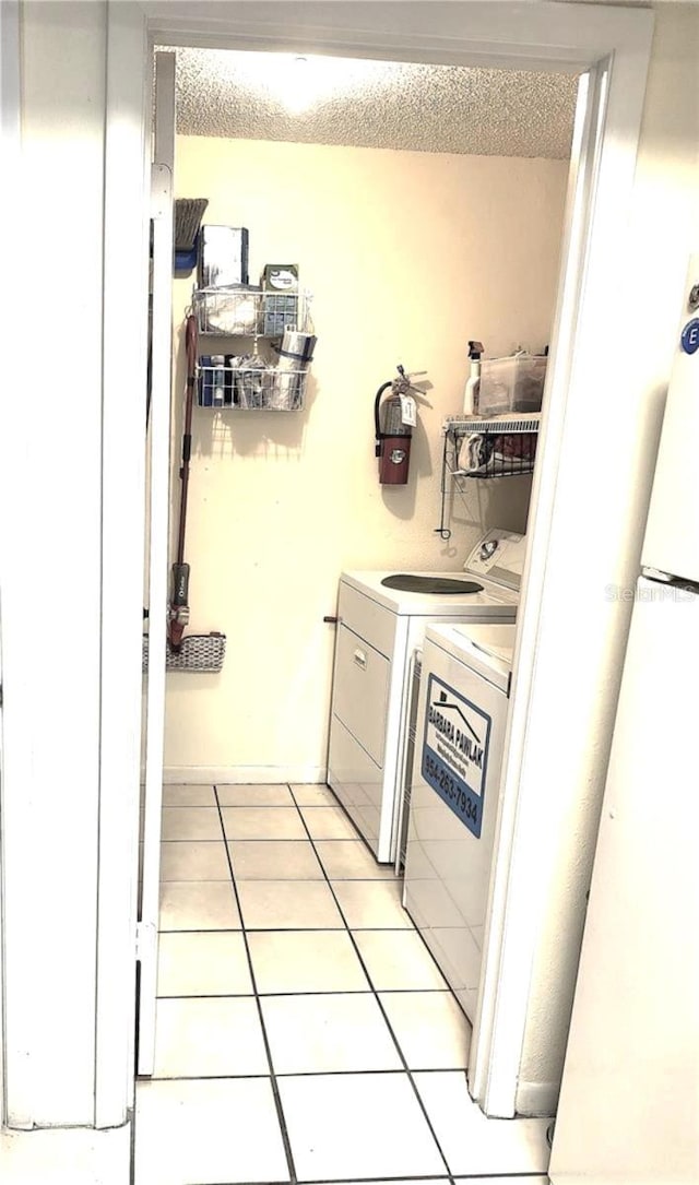 clothes washing area featuring washing machine and dryer, light tile patterned flooring, and a textured ceiling