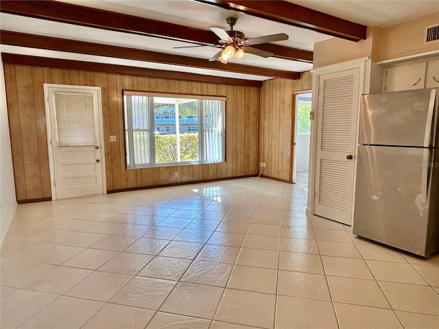 interior space featuring wood walls, light tile patterned flooring, beam ceiling, and stainless steel refrigerator