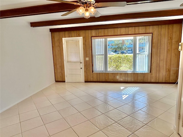 tiled empty room with beamed ceiling, ceiling fan, and wooden walls