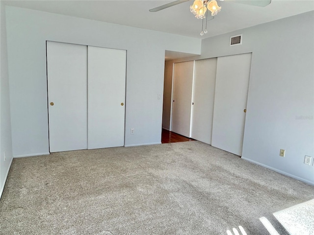 unfurnished bedroom with ceiling fan, carpet floors, and two closets