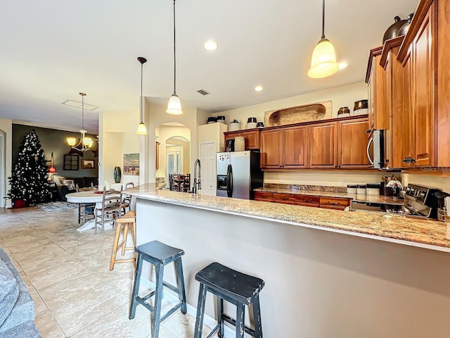 kitchen featuring light stone countertops, kitchen peninsula, decorative light fixtures, a breakfast bar, and appliances with stainless steel finishes